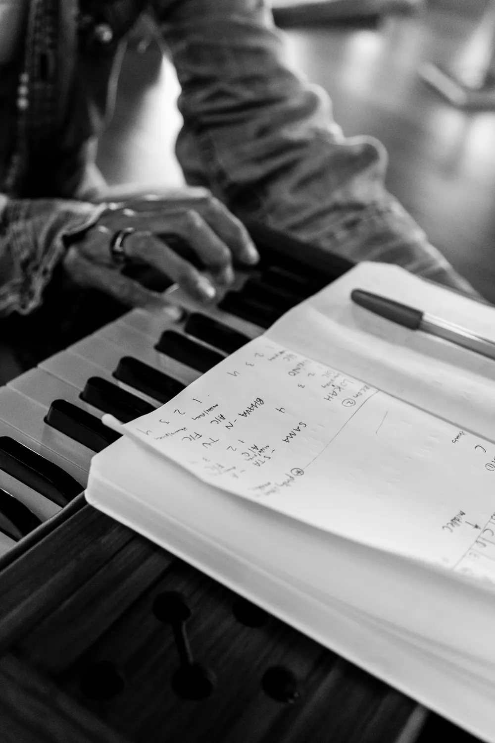 Closeup of hands playing a harmonium with a notebook and pen