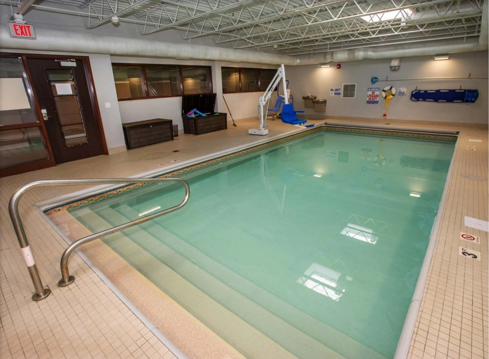 Spacious and accessible indoor swimming pool at Flatrock residences, featuring a chair lift, safety equipment, and welcoming amenities for resident recreation and 24/7 supervised relaxation in renovated homes.