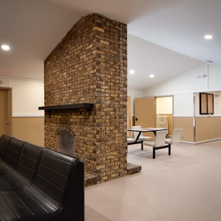 Cozy common living room with brick fireplace, bench seating, and dining table at Flatrock Facility residential care home for mental health and recovery support