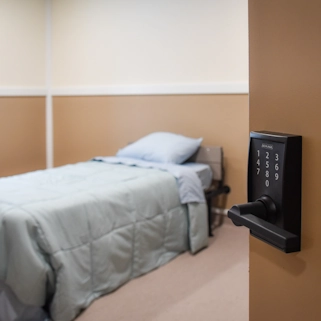 Private secure bedroom with bed, blue bedding, and keypad lock door in Flatrock Facility adult foster care residence for comfortable mental health treatment
