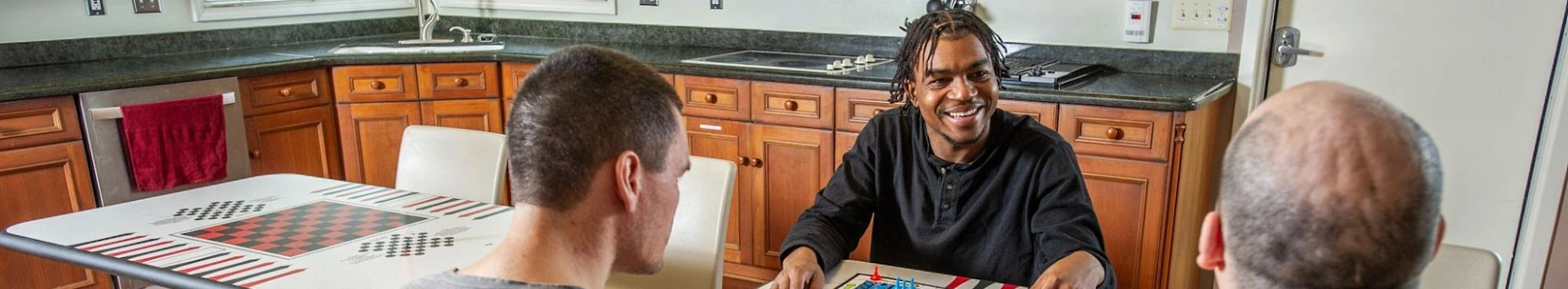 Residents socializing and playing board games at a table in a fully equipped communal kitchen.