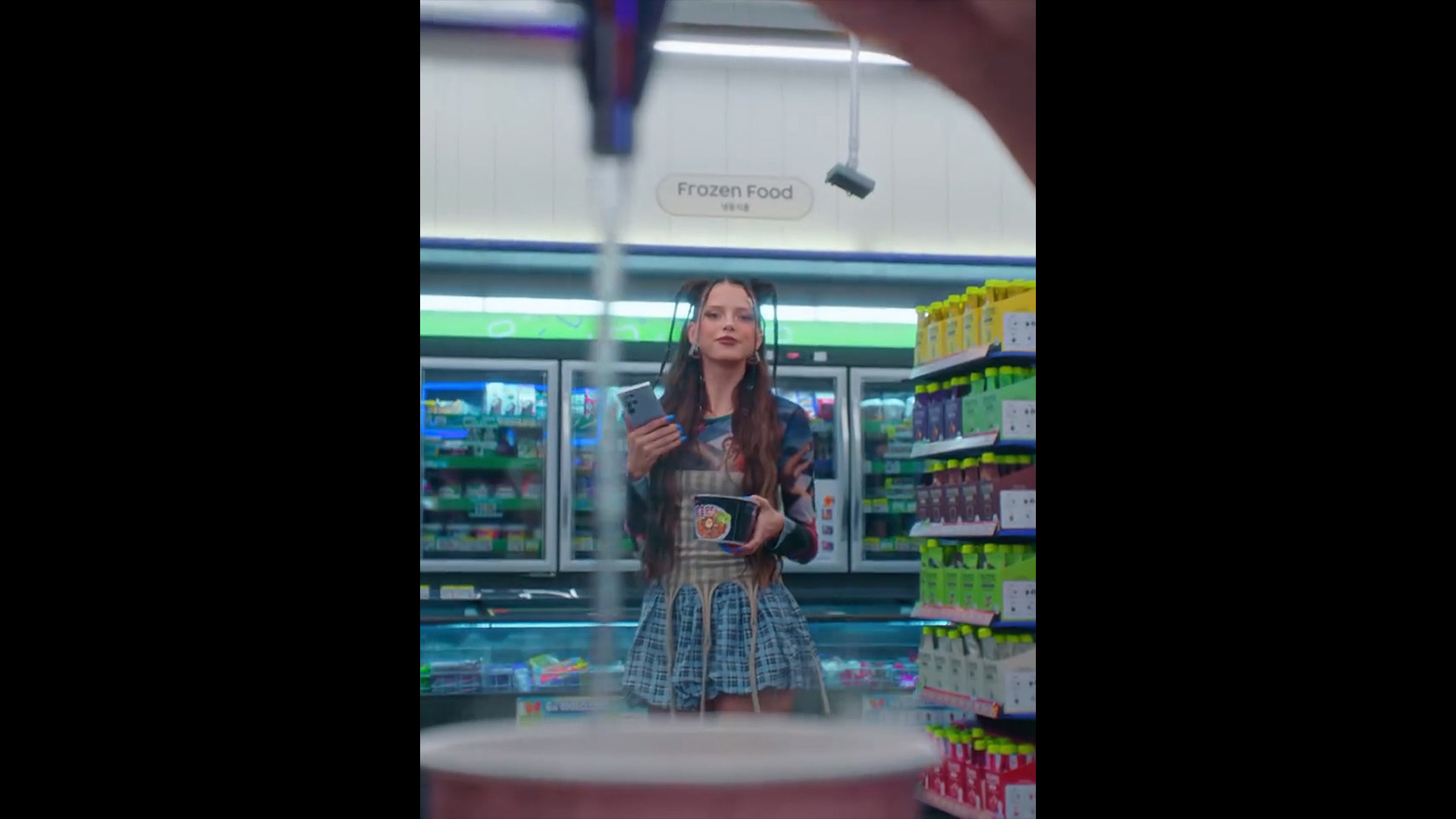 편의점 안, 라면에 물을 붓는 모습을 바라보며 서 있는 니나 츄바 / Nina Chuba standing inside a convenience store, watching someone pour hot water into instant noodles