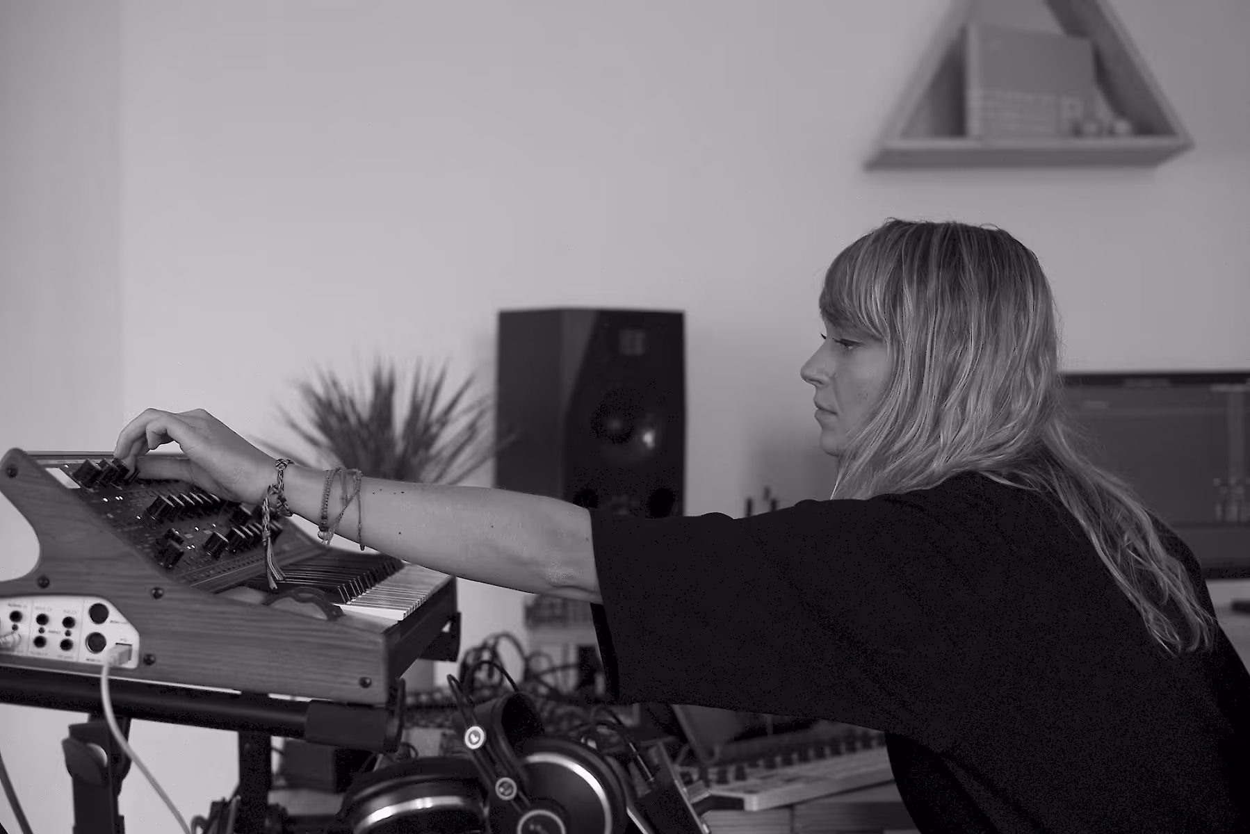 Nadia Struiwigh adjusting knobs on a synthesizer in a home studio setting. She is focused on her work, with headphones and various music equipment around her, creating a serene and creative atmosphere.