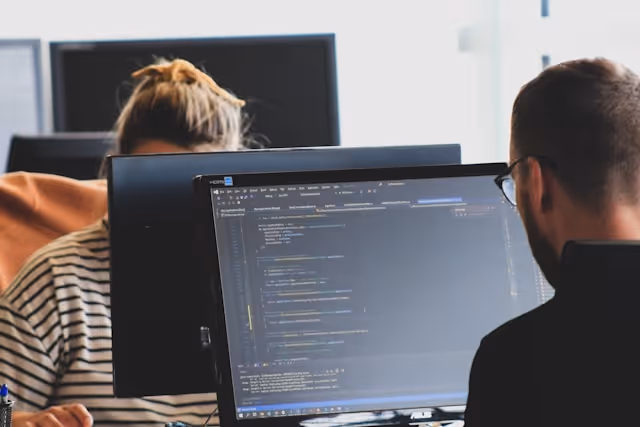 Two people work on computers with code displayed on the screen.