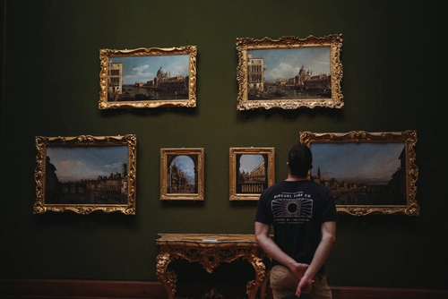 Visitante observa seis cuadros enmarcados en una galería de paredes oscuras.