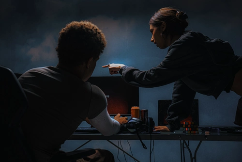 Dos personas trabajando en una computadora en una atmósfera oscura.