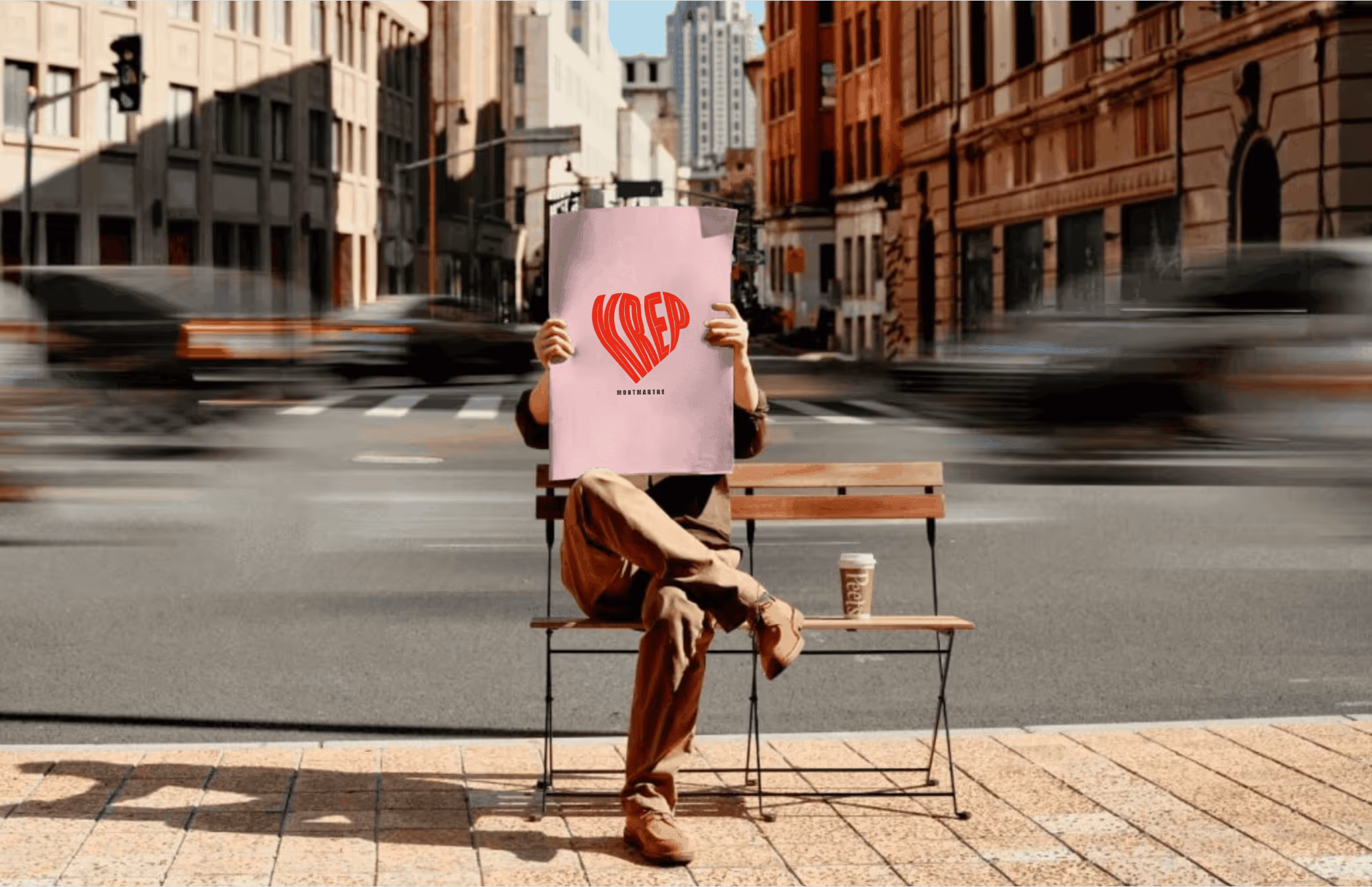 Personne assise sur un banc et lisant un grand journal rose, avec un café posé à côté.