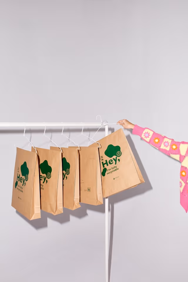 Quatre sacs en papier recyclable suspendus devant un fond gris clair.