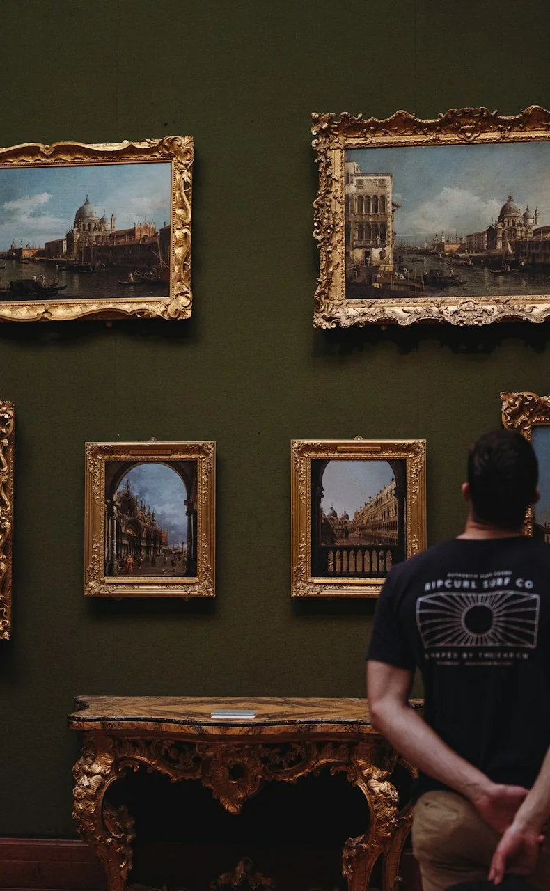 Visiteur observant six tableaux encadrés dans une galerie aux murs sombres.