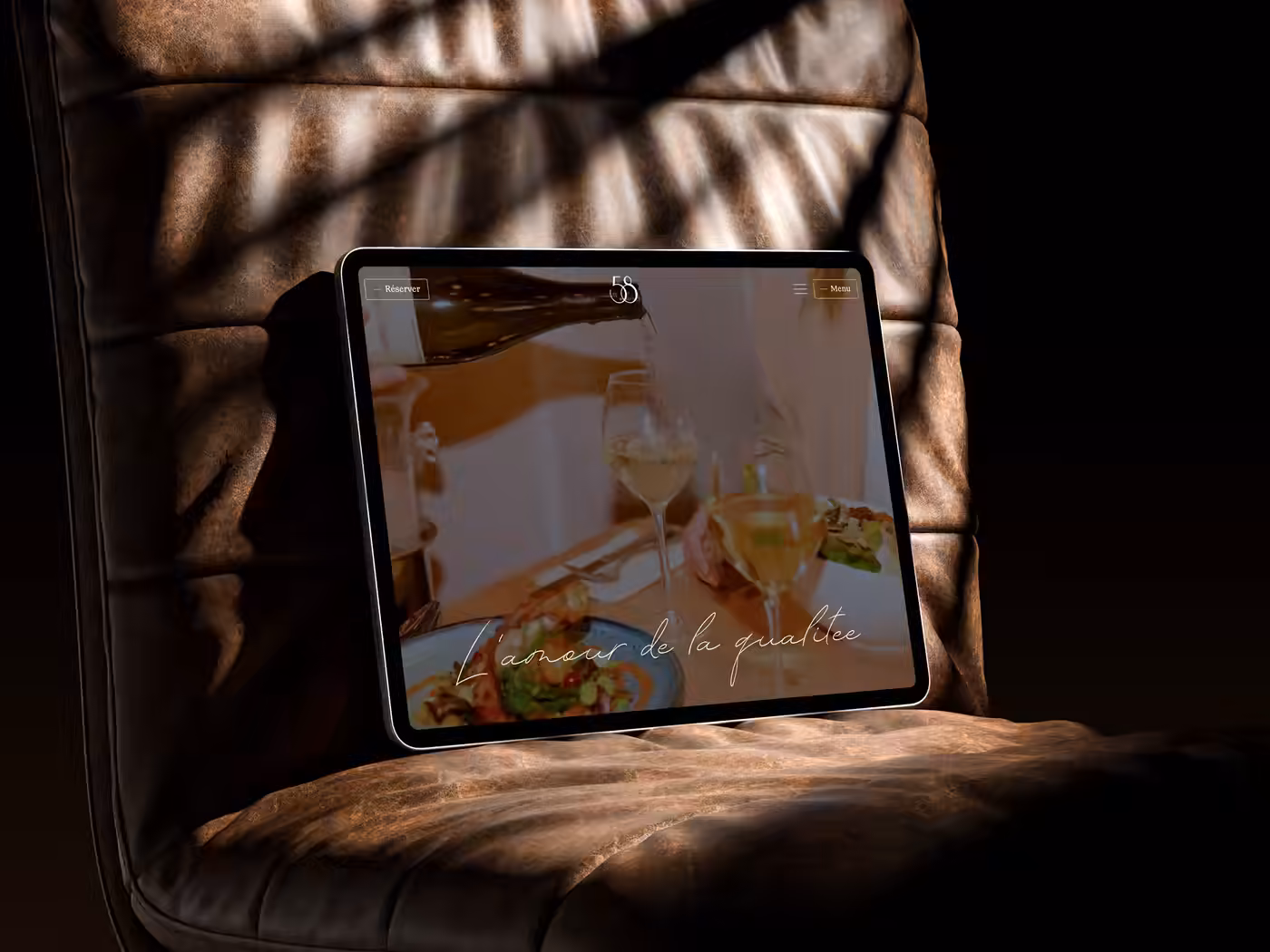 Tablette affichant un verre de vin blanc versé à côté d’un plat gastronomique, posée sur un fauteuil en cuir.