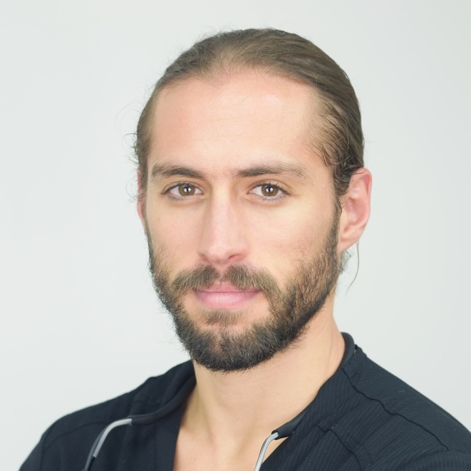 Man with light brown hair tied back and beard wearing a black medical scrub top with stethoscope.