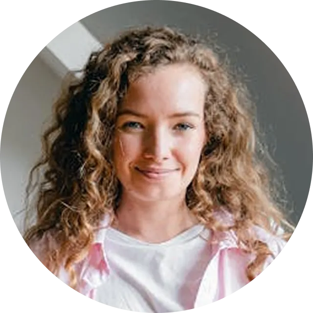 Young girl with curly brown hair wearing a white and pink striped shirt, smiling at camera
