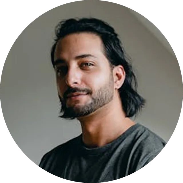 Man with long dark hair and beard wearing a gray t-shirt against a neutral gray background