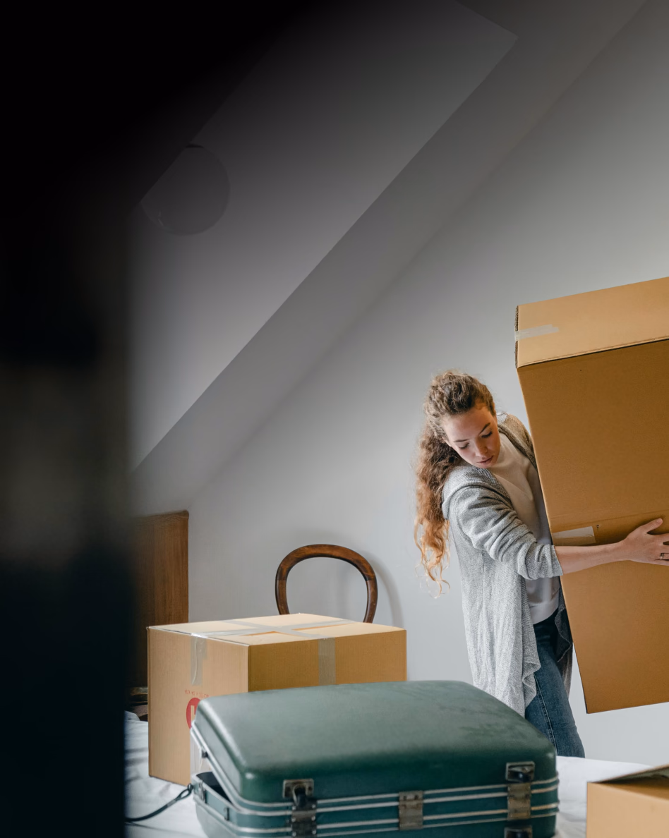 Woman packing cardboard boxes and vintage suitcase in bright attic space