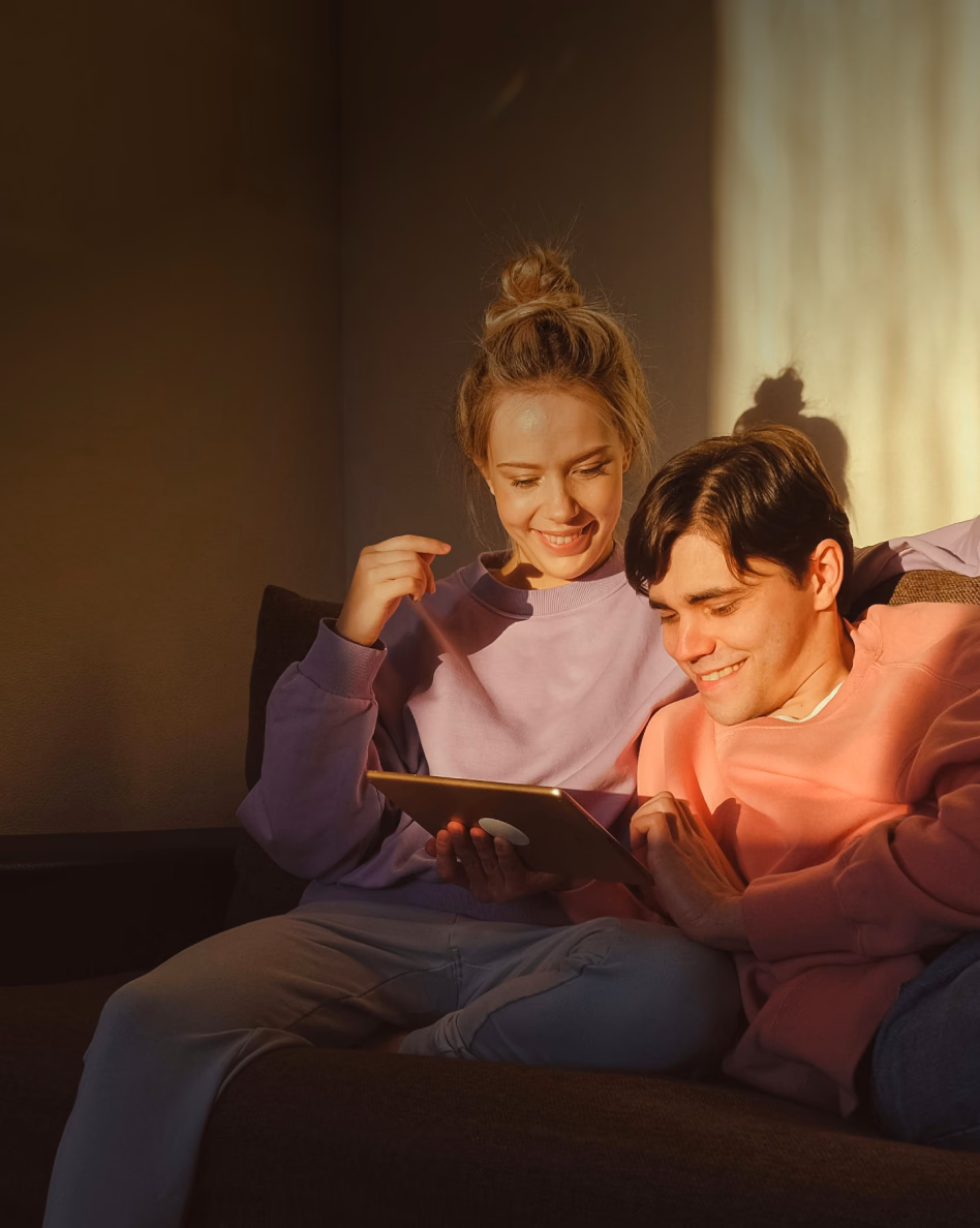 Two children sitting together on a couch looking at a tablet device