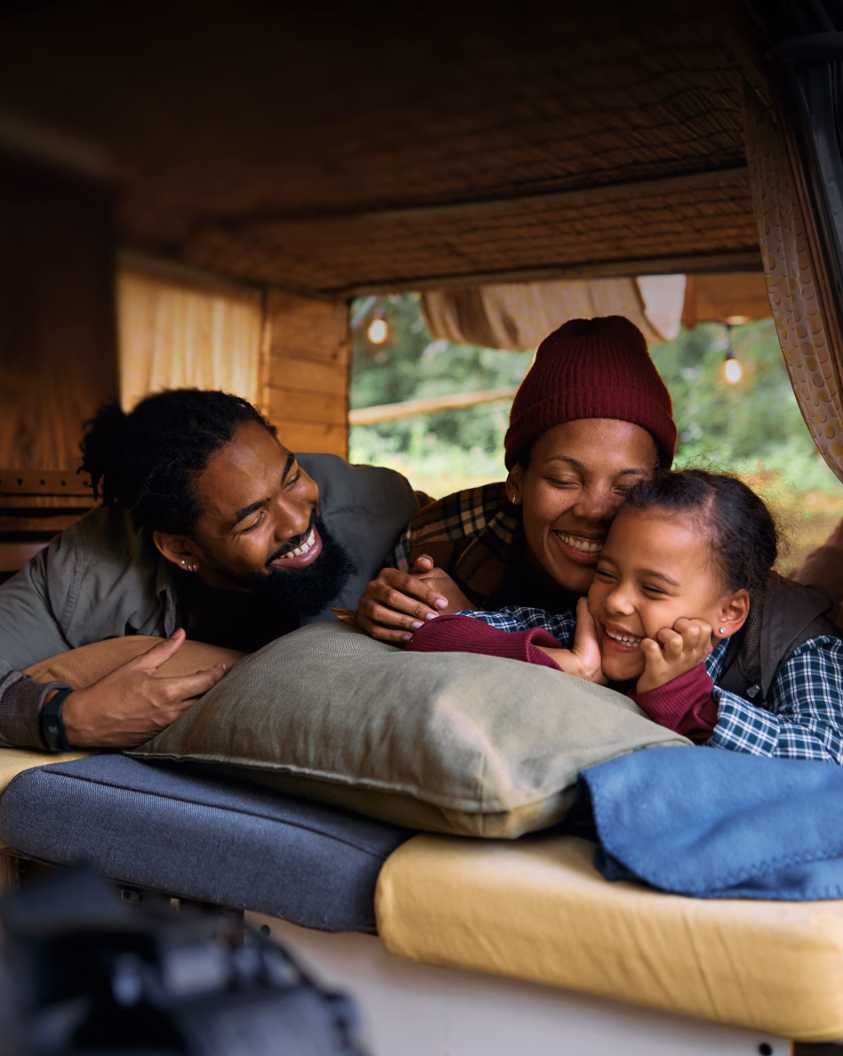 A smiling family of four relaxes together on a bed in a cozy cabin interior