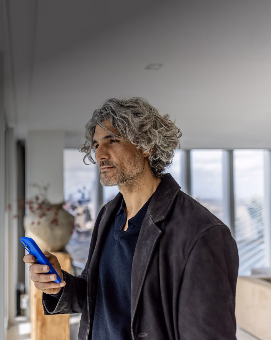 Man with gray hair holding a blue phone in a modern office space with large windows