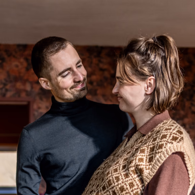 Two people facing each other in conversation against a brick wall background