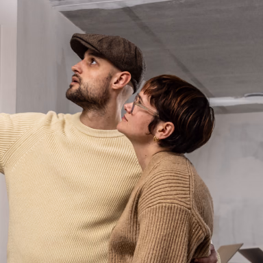 Two people in neutral-toned sweaters looking upward together in an interior space