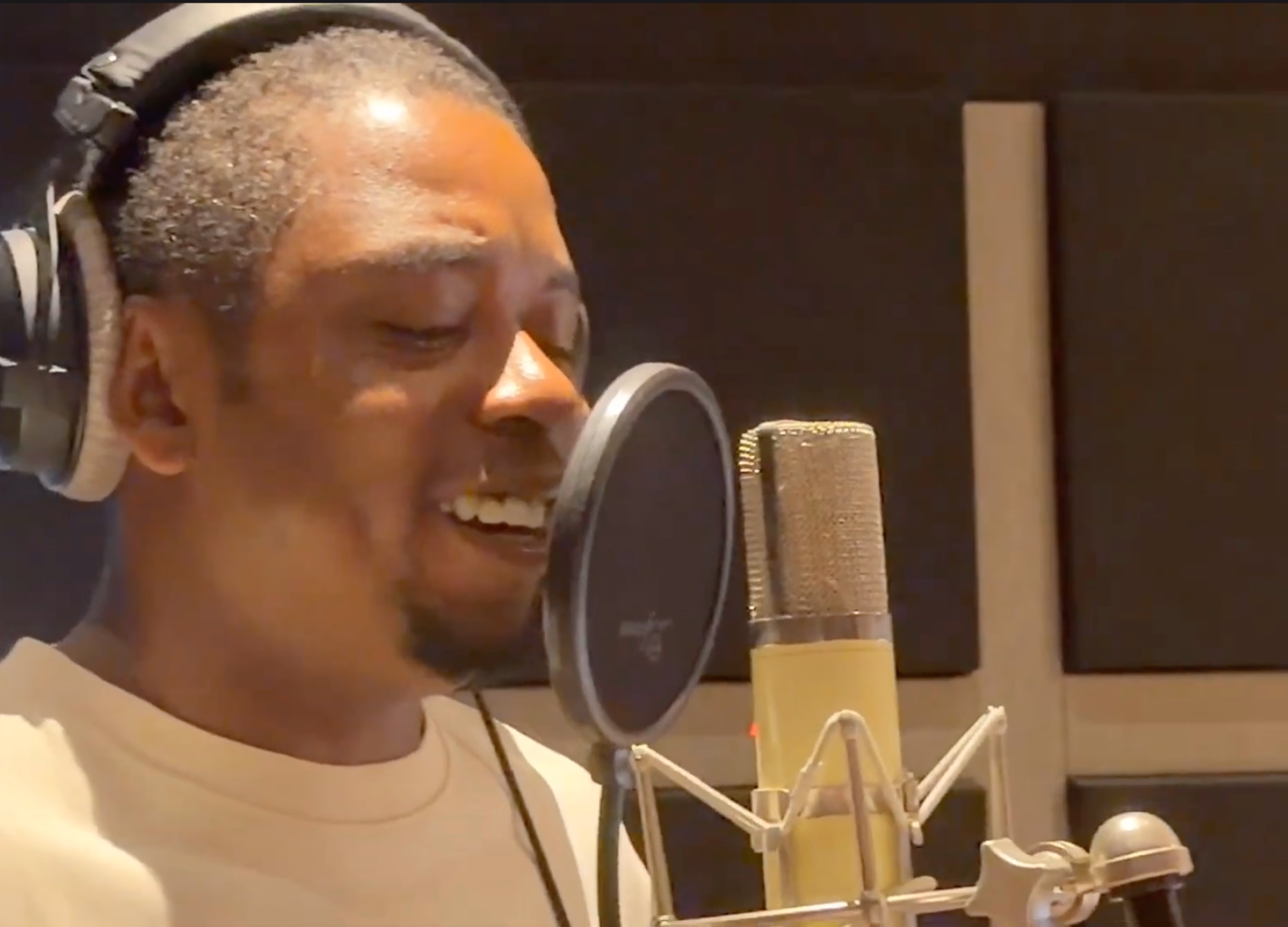 Male vocalist singing into a studio microphone while wearing headphones in a recording studio