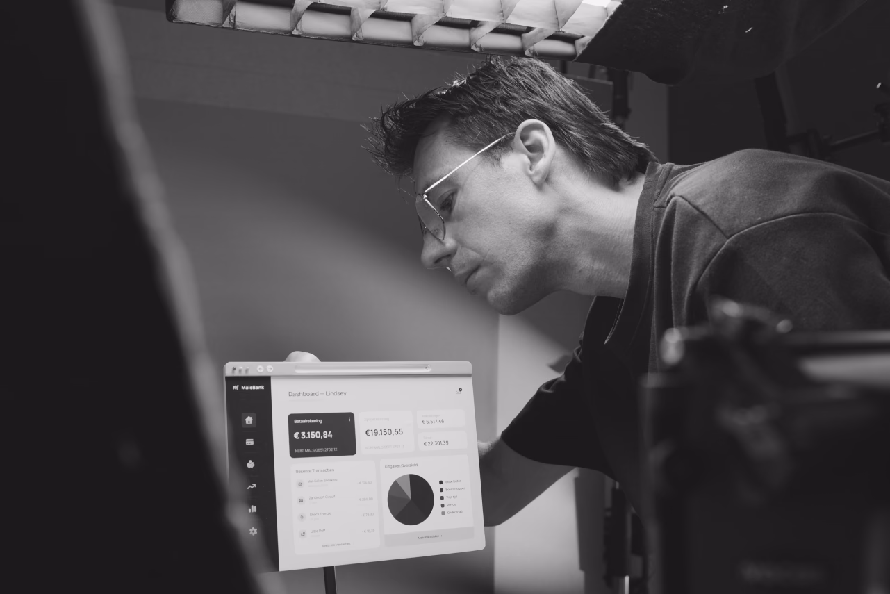 Man wearing glasses examines a digital display panel with charts and data metrics in a studio setting
