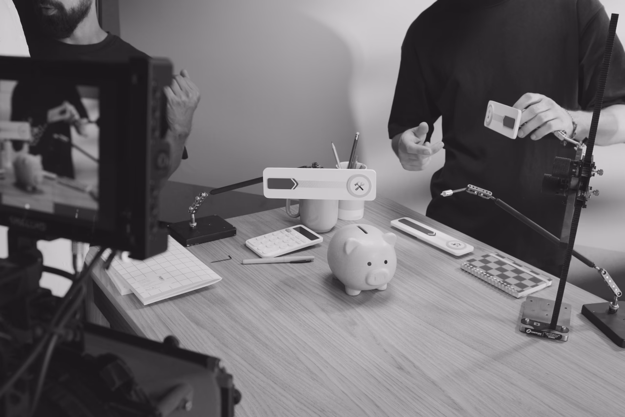 Two people at a desk with a piggy bank, microphone, and recording equipment during a podcast or media recording session
