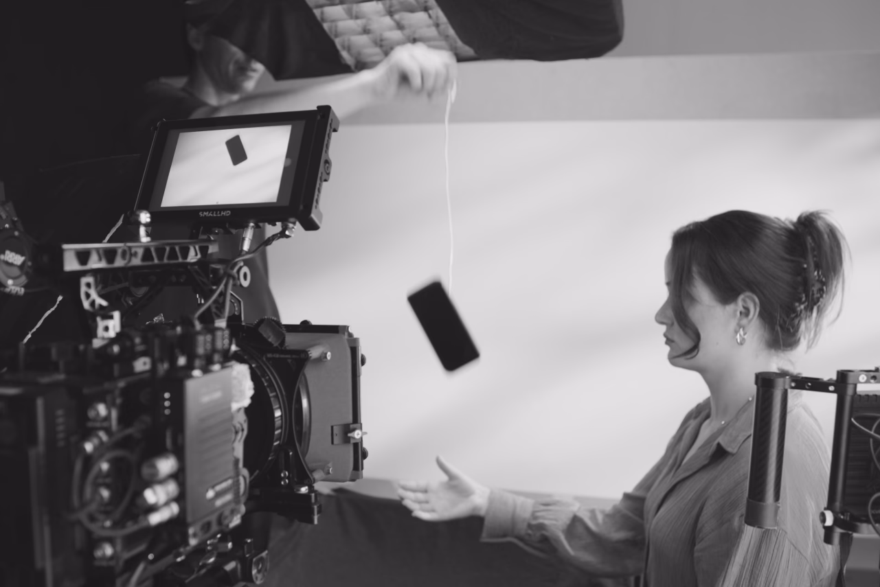 Film crew member adjusting lighting equipment while woman operates professional camera on set