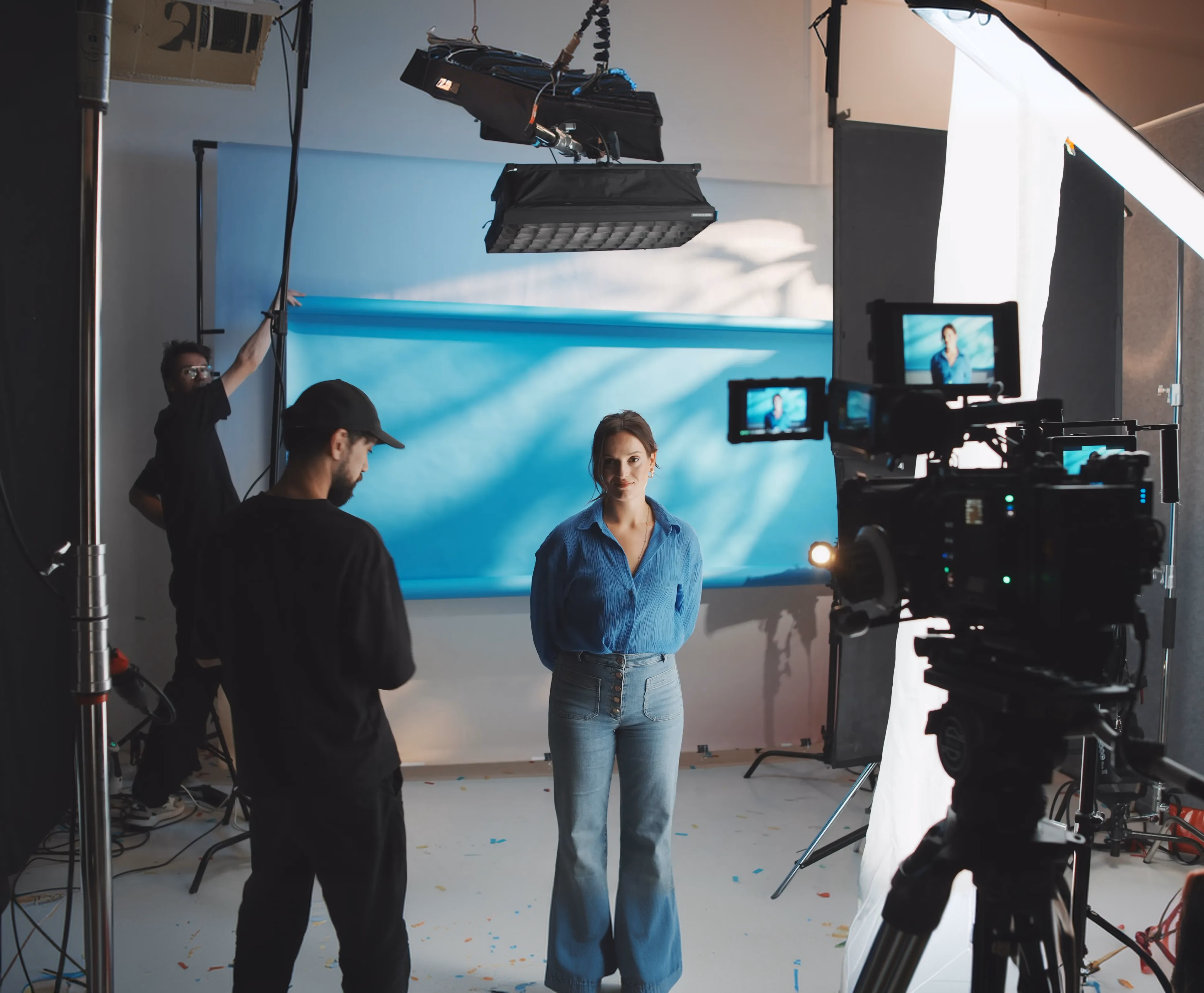 Film crew shooting a woman against a blue ocean backdrop in a professional studio setting