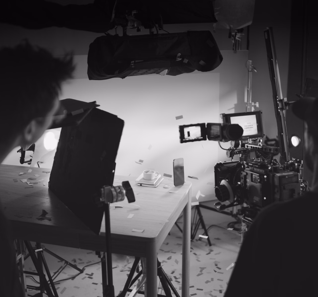 Black and white studio setup with lighting equipment, camera on tripod, and white table with scattered objects