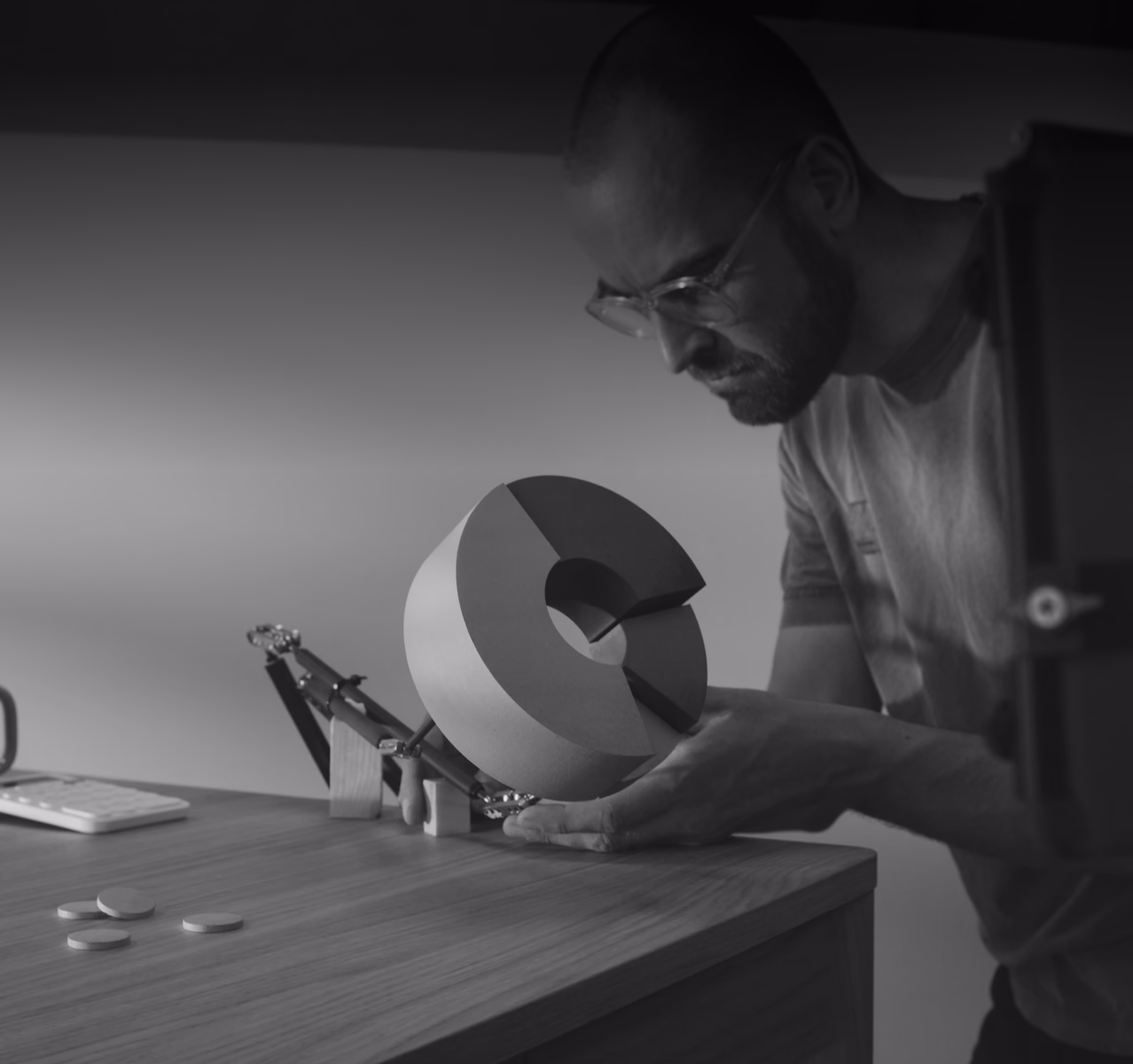 Person wearing glasses examining a circular geometric object on a wooden table