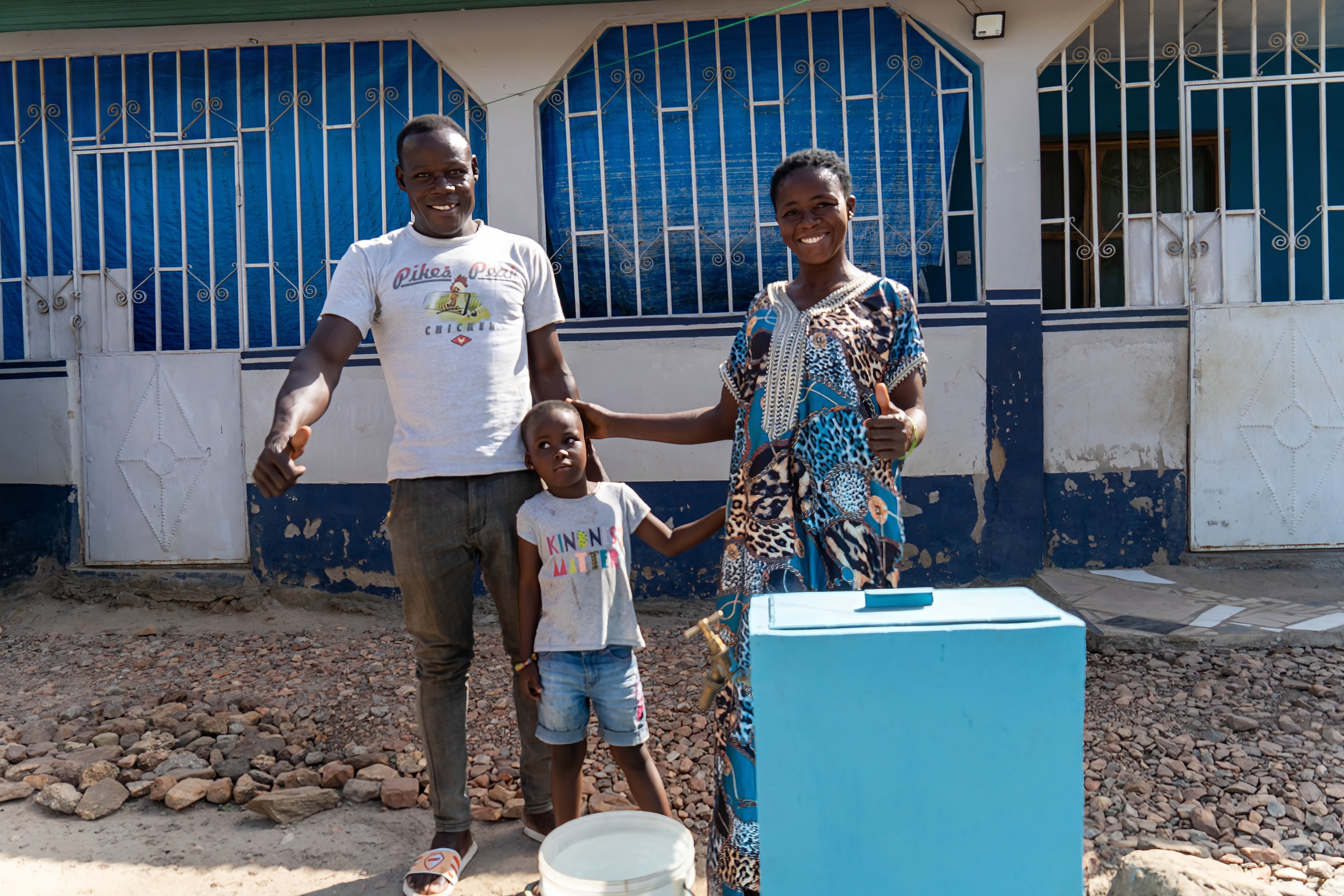 A family in Ghana smile next to their NUMA Now safe water connection at home.