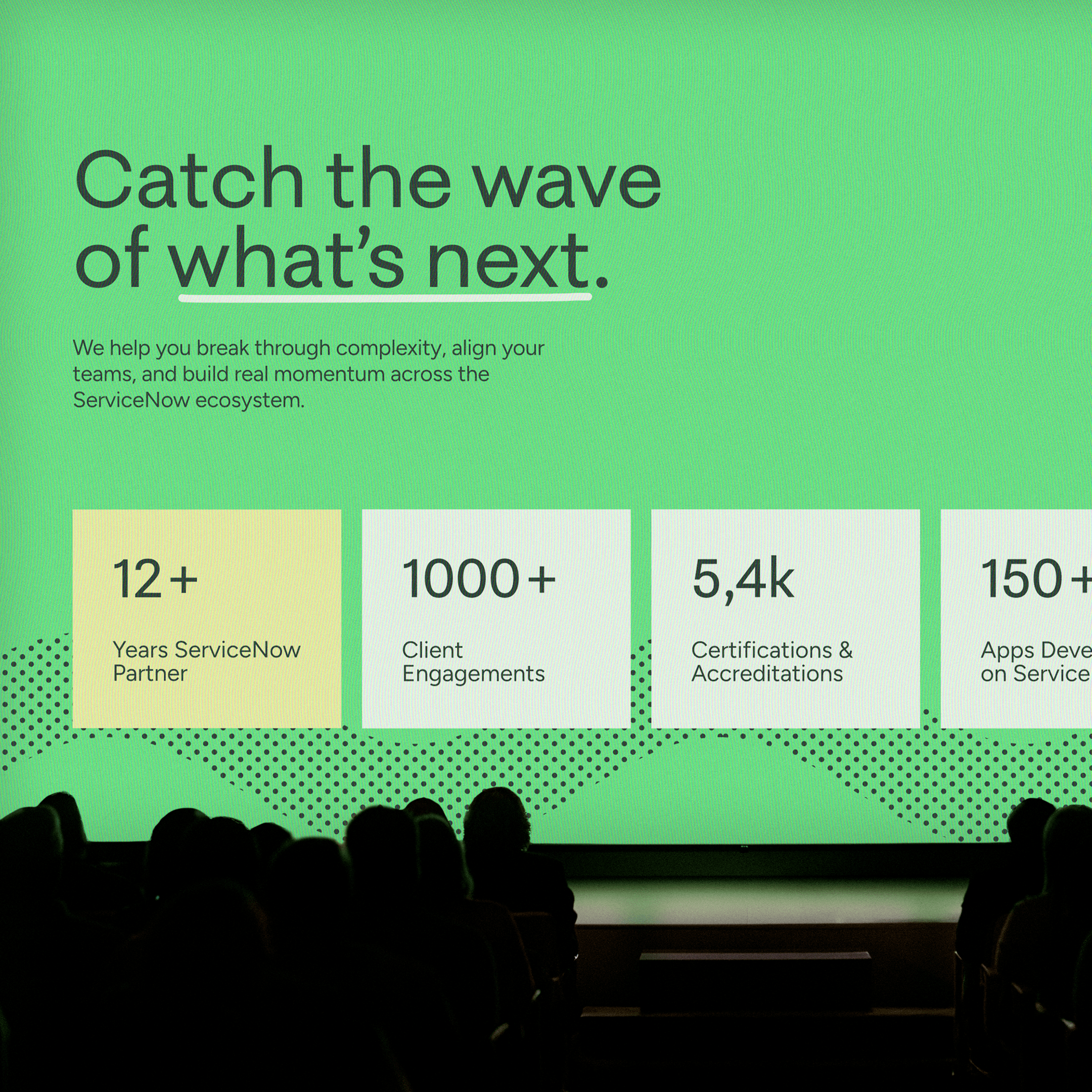 Presentation slide with green background and bold text reading 'Catch the wave of what’s next.' followed by statistics about ServiceNow partnership, client engagements, certifications, and app development, with audience silhouettes in foreground.