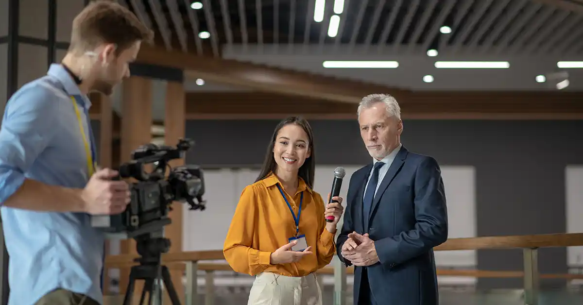 Jornalista entrevista executivo durante gravação em vídeo, representando assessoria de imprensa e construção de autoridade na mídia.