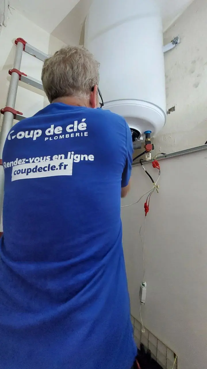 Plombier debout de dos en t-shirt bleu qui répare un chauffe-eau en hauteur