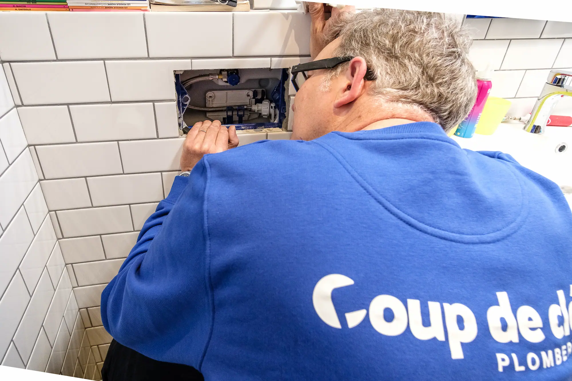 Plombier portant une t-shirt bleu réparant le mécanisme d'un WC suspendu