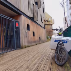Vélo cargo avec boîte blanche portant le logo ChronoKitchen garé sur un trottoir en bois à côté d'un bâtiment moderne.