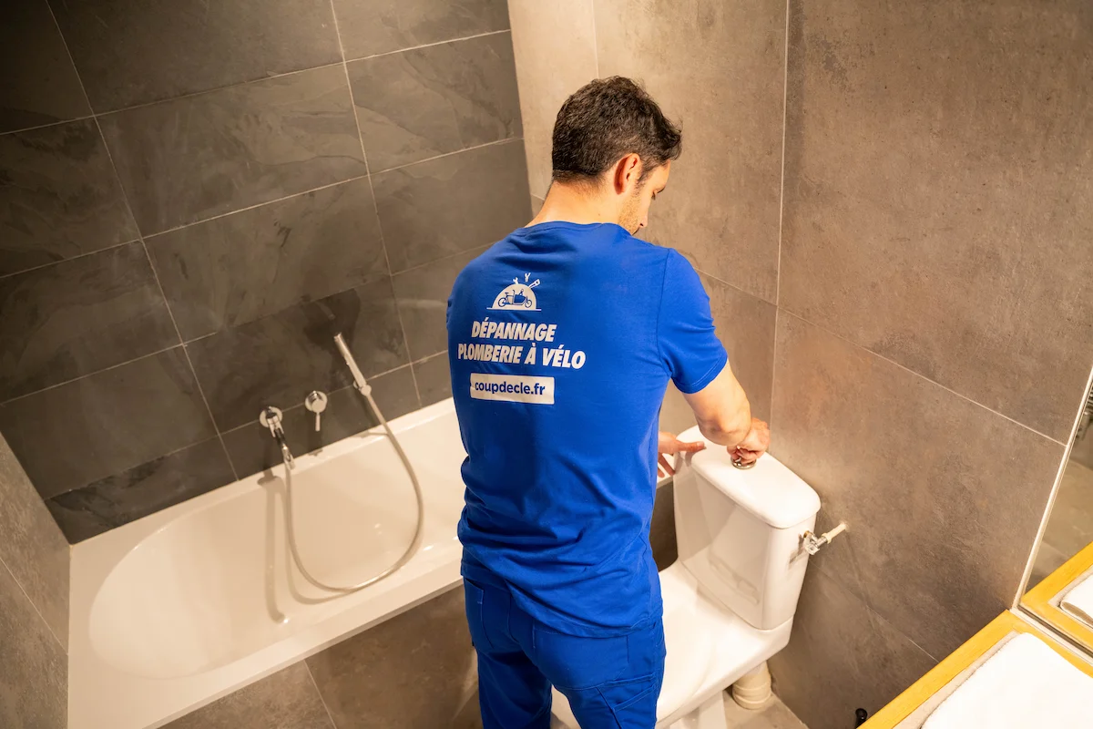 Homme en t-shirt bleu réparant des toilettes, dépannage professionnel plomberie