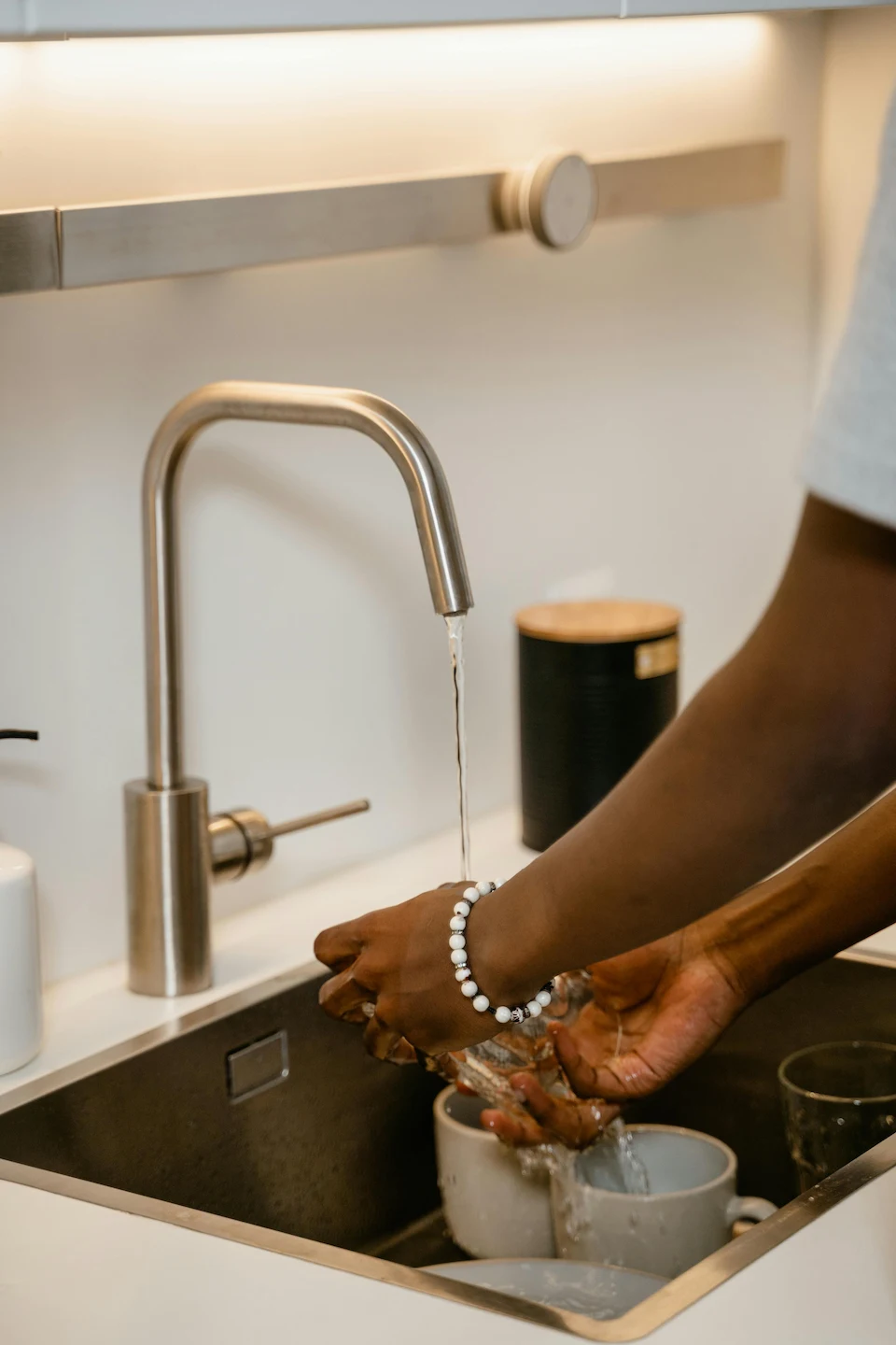 Personne se lavant les mains dans une cuisine moderne, évier et robinets en acier inoxydable