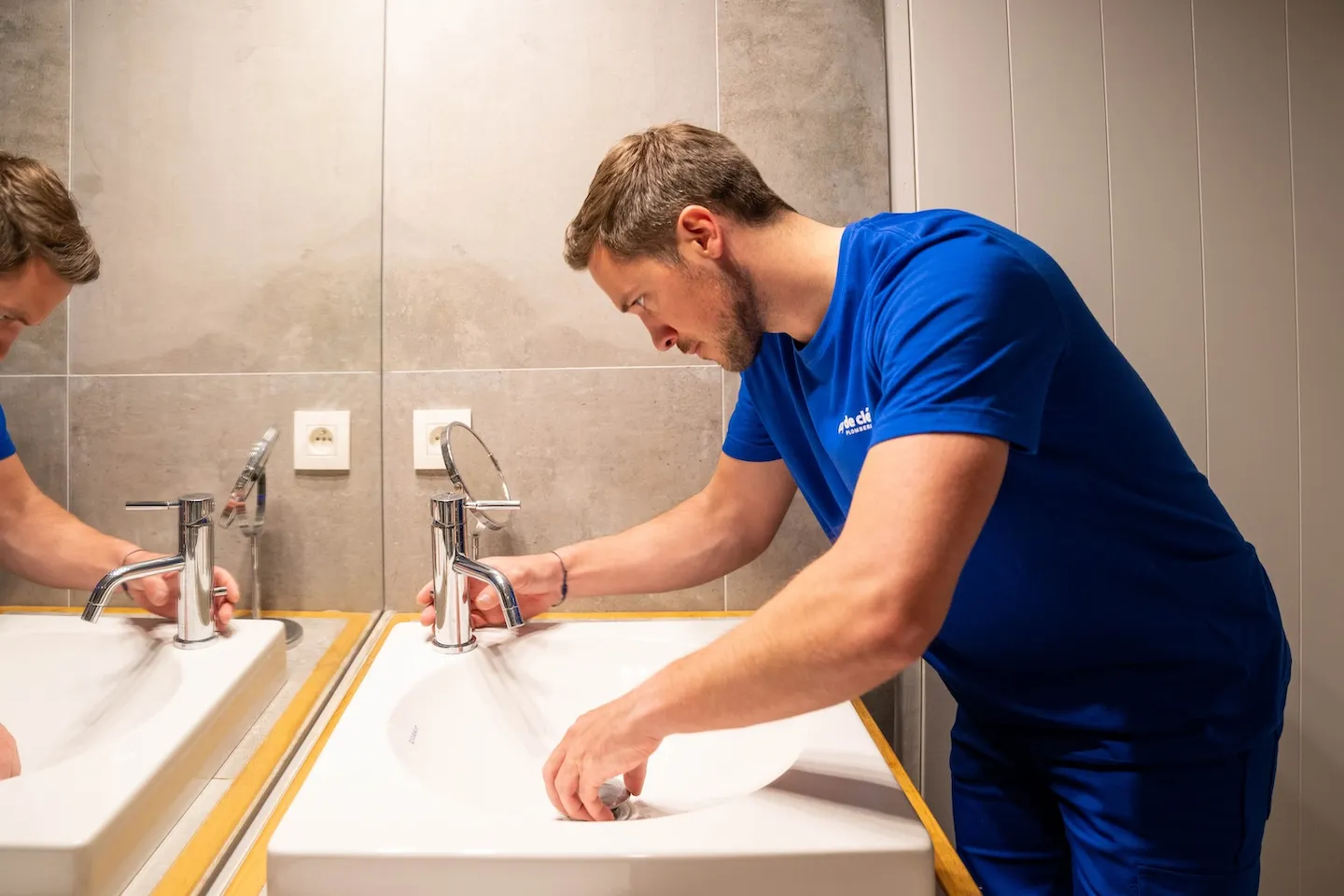 plombier réparant un robinet mitigeur de lavabo de salle de bain moderne, t-shirt bleu