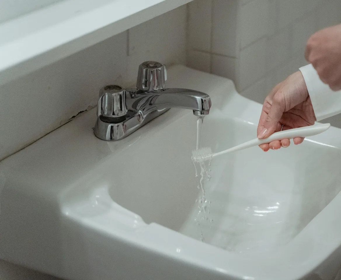 Personne se brossant les dents en faisant couler l'eau d'un robinet de lavabo de salle de bain