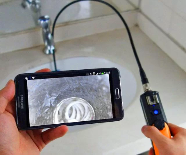 Personne tenant un smartphone connecté à une caméra et visualise une canalisation