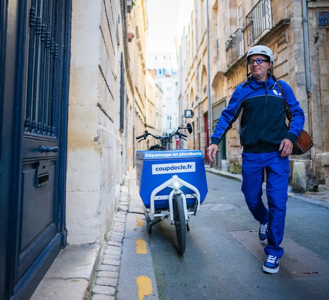 Plombier Coup de clé marchant dans une rue de Bordeaux à côté de son vélo vargo