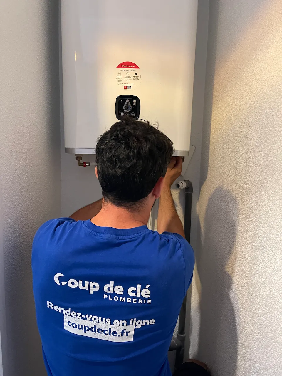 Homme en t-shirt bleu effectuant la réparation d'un chauffe-eau électrique plat, maintenance plomberie