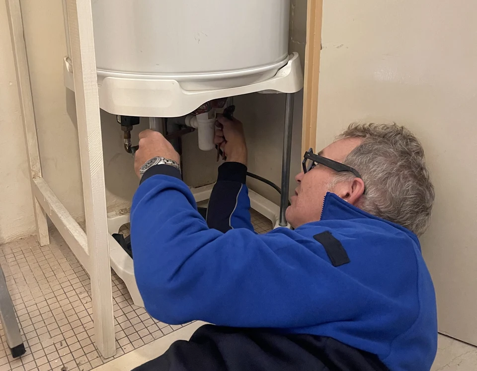 Homme effectuant une maintenance sur un chauffe-eau électrique dans une installation domestique