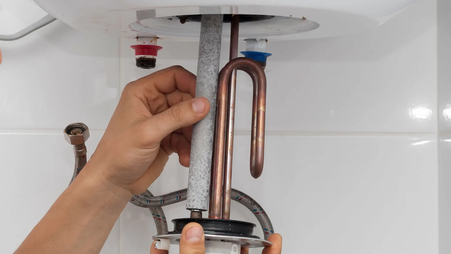 Main d'une personne tenant une anode et une résistance de chauffe-eau électrique