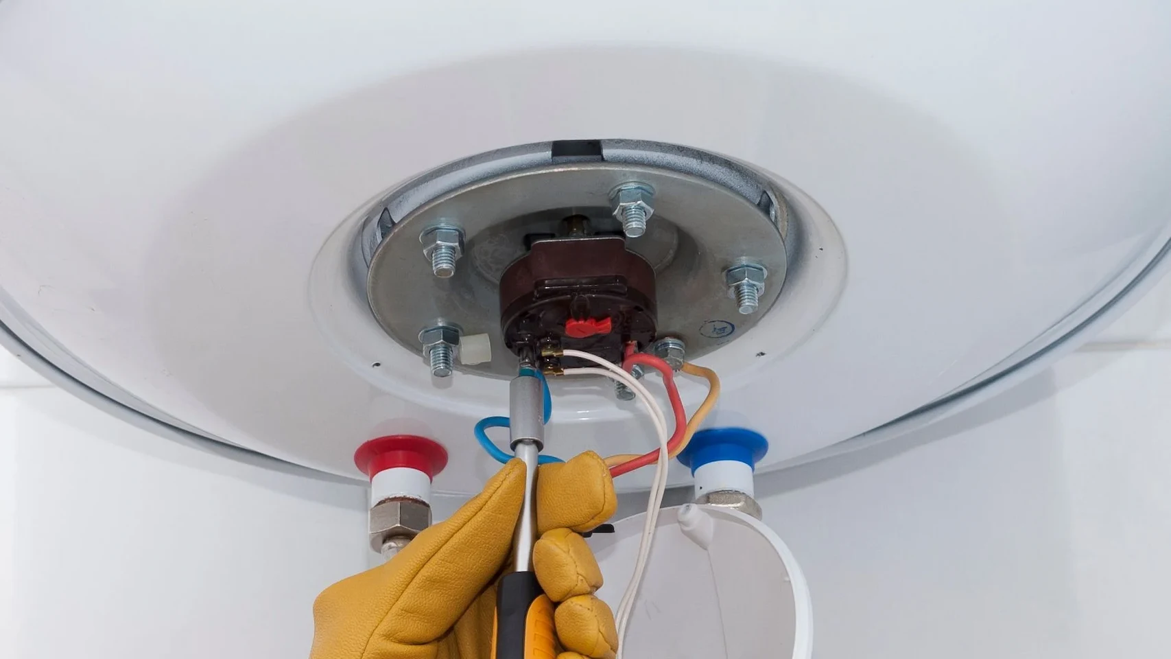 Main sur fond neutre tenant un thermostat sous un ballon d'eau chaude