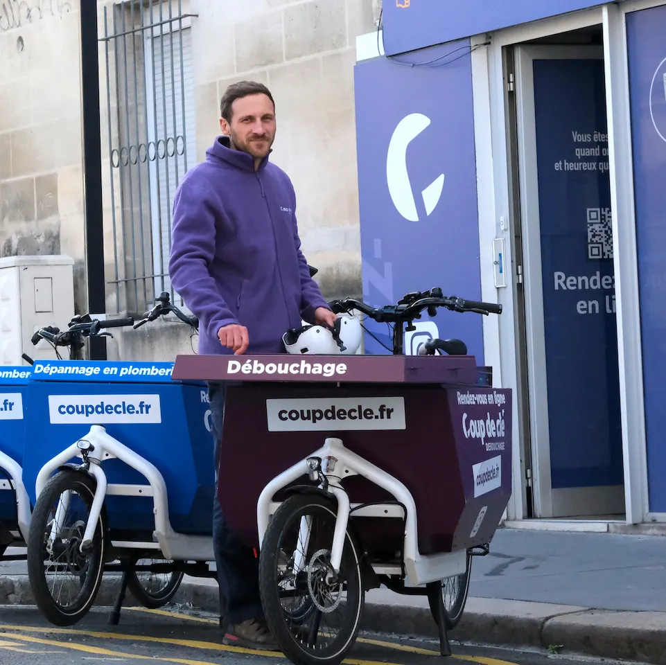 L'équipe Coup de clé Plomberie debout à côté d'un vélo discutant dans une rue bordelaise, style décontracté