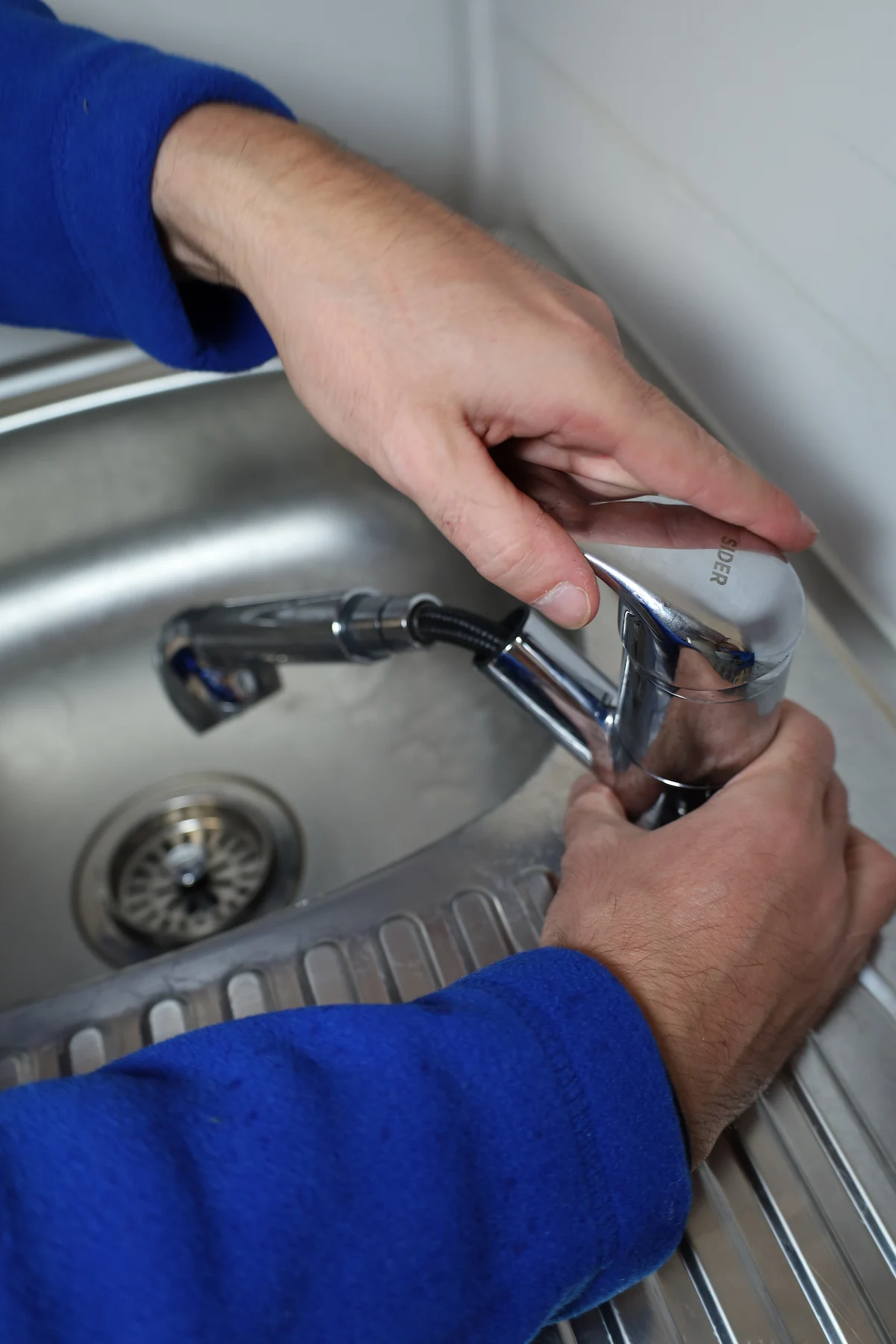 Mains d'une personne ajustant un robinet de cuisine chromé au-dessus d'un évier métallique.