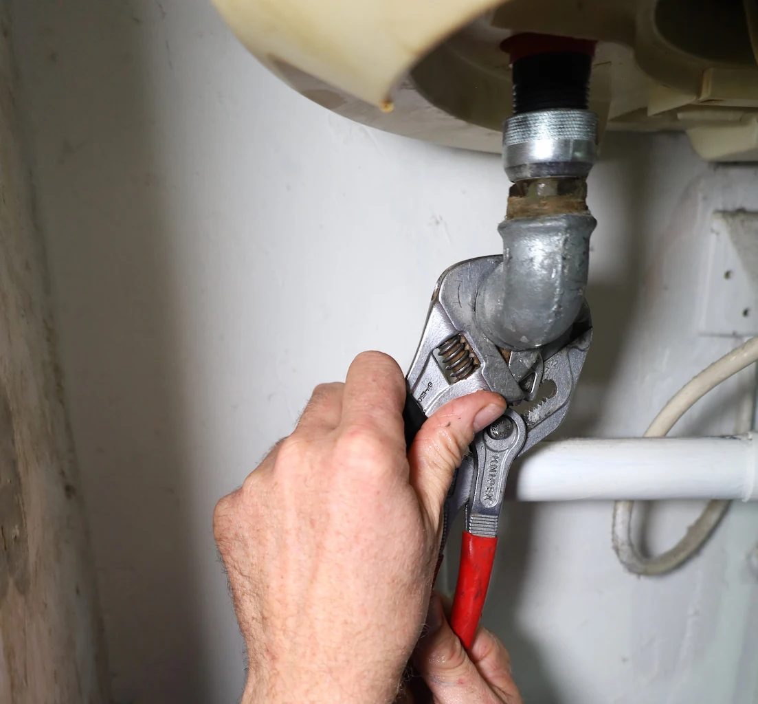 Main serrant un tuyau métallique avec une clé à molette sous un chauffe-eau.