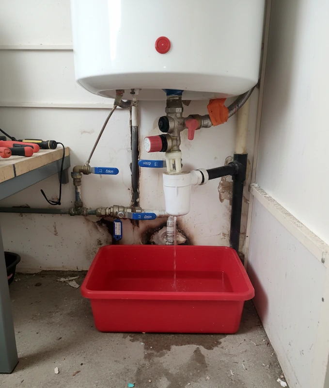 Un chauffe-eau blanc avec une fuite d'eau s'écoulant dans un bac rouge placé en dessous.